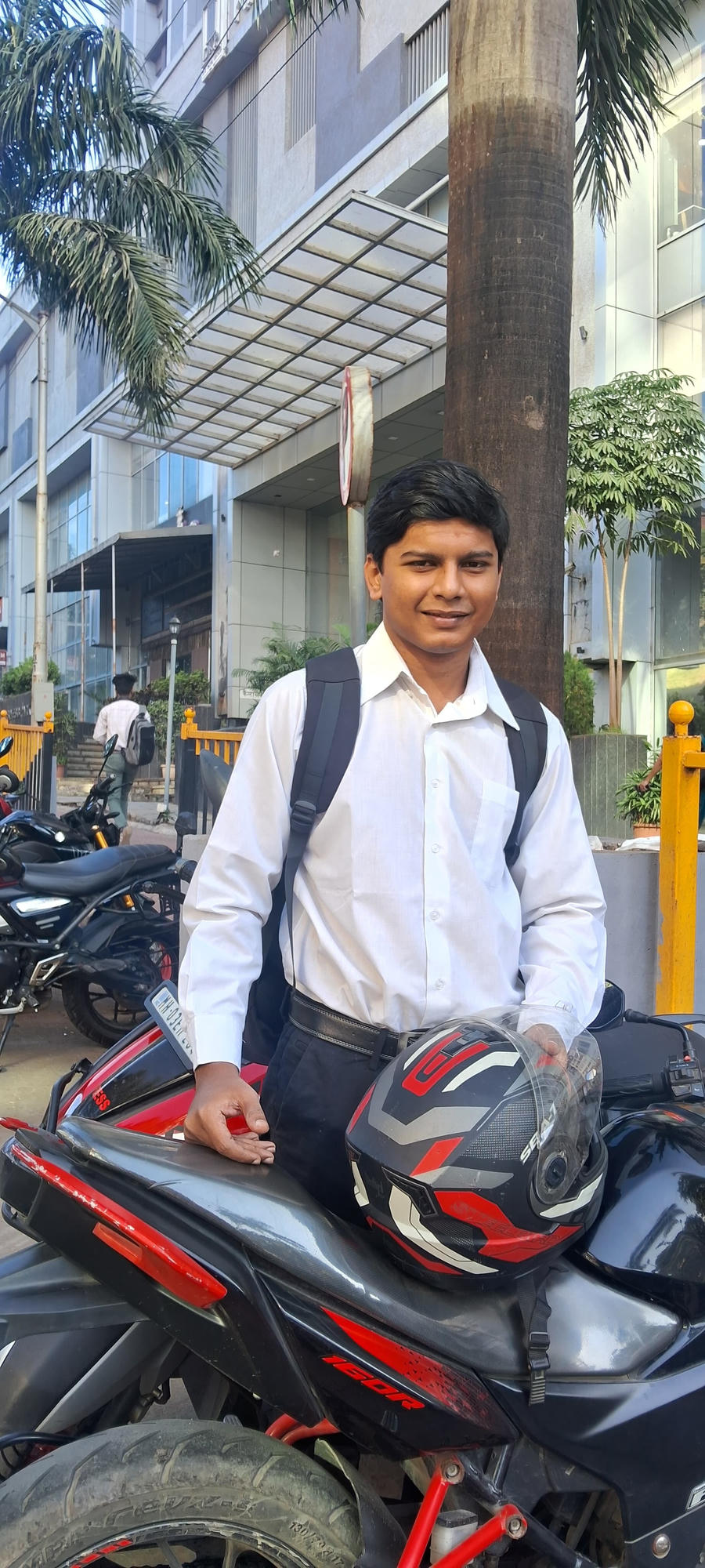 Soham in a white shirt standing beside a motorcycle outside a building